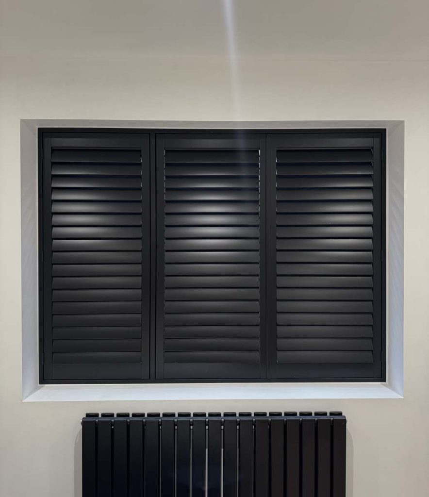 Black window shutters fitted in a modern interior above a radiator in a UK home
